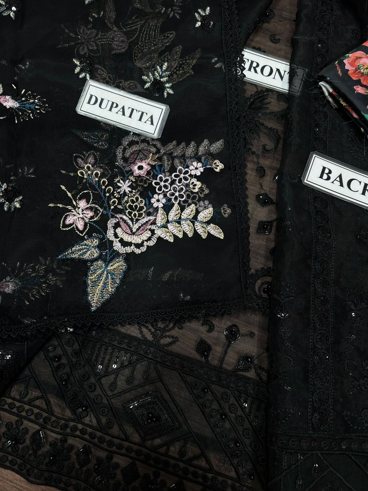 Black embroidered garment with brand labels on a dark background