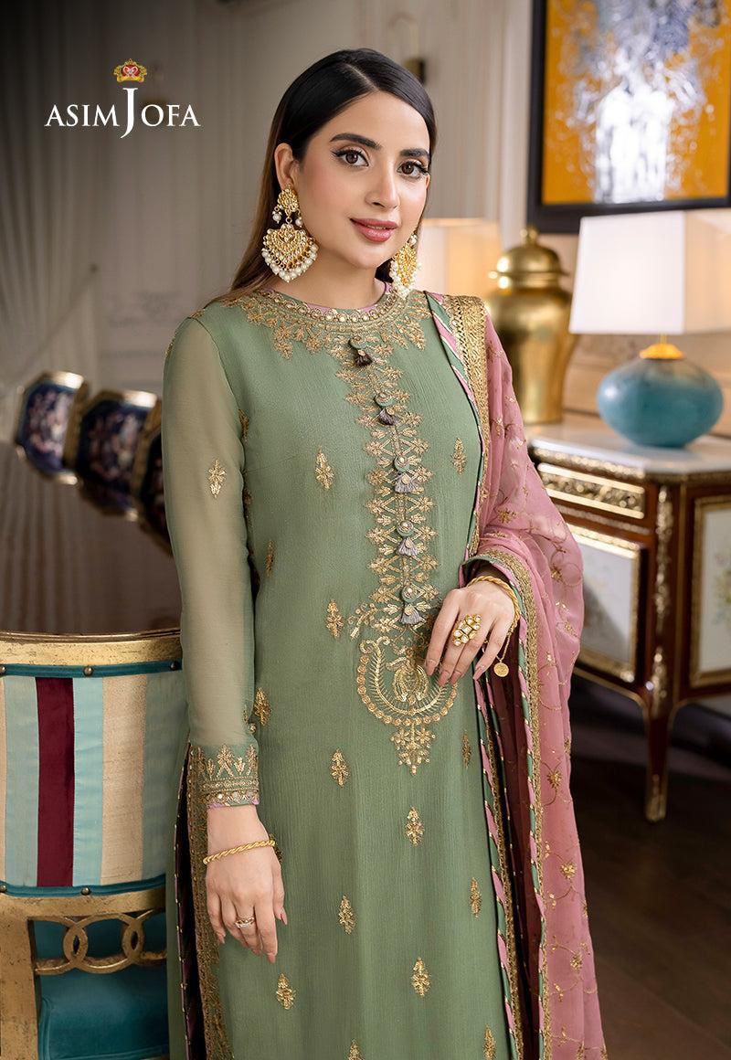 Woman in a green embroidered traditional outfit with pink dupatta in an elegant room.