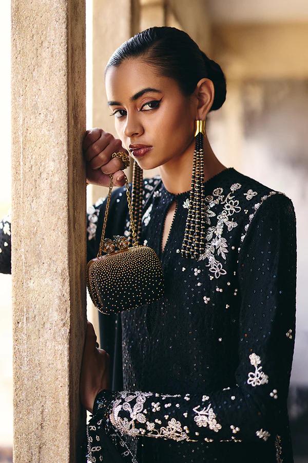Woman in a black embroidered outfit holding a beaded handbag.