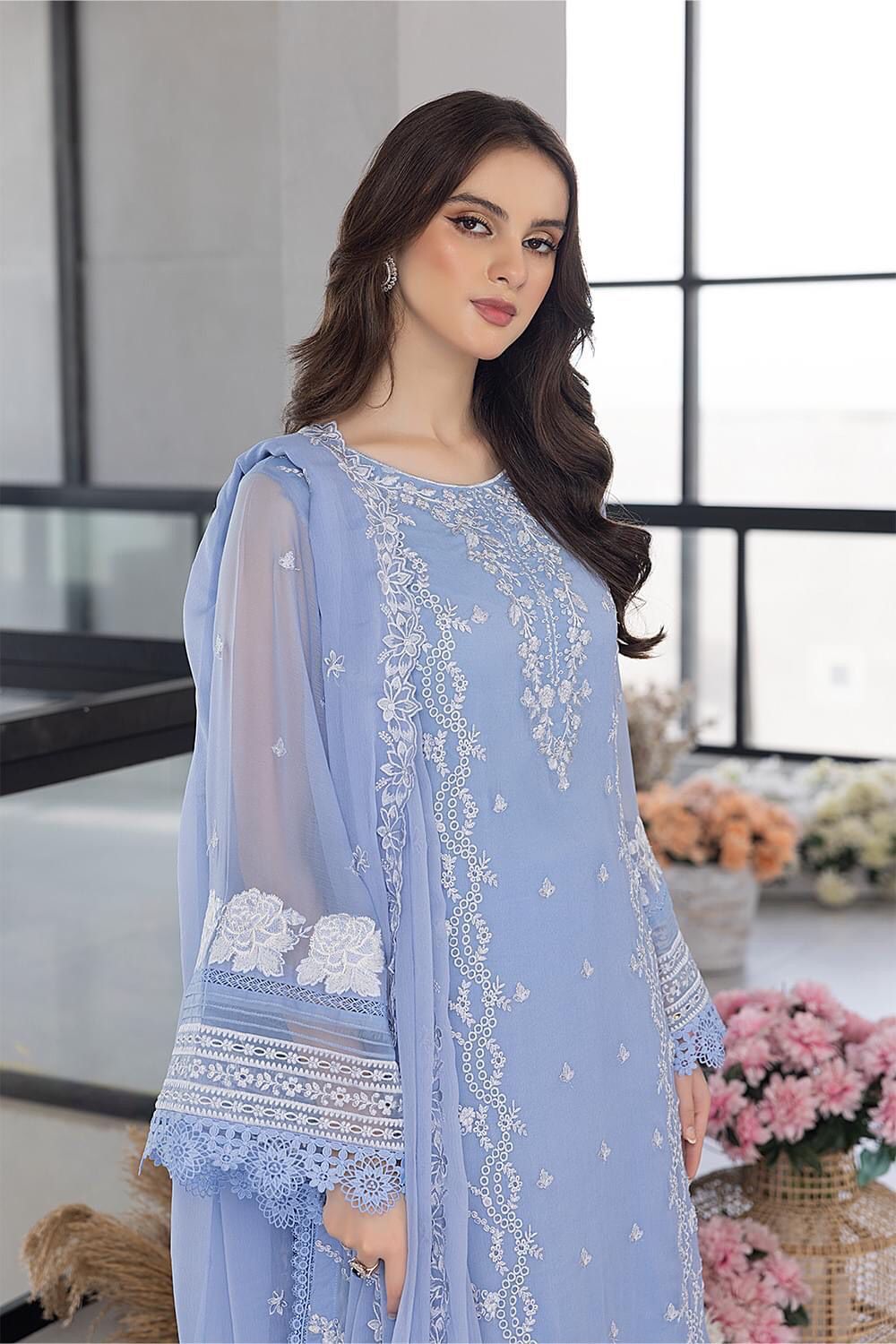 Woman wearing a light blue embroidered dress in an indoor setting with flowers and decor.
