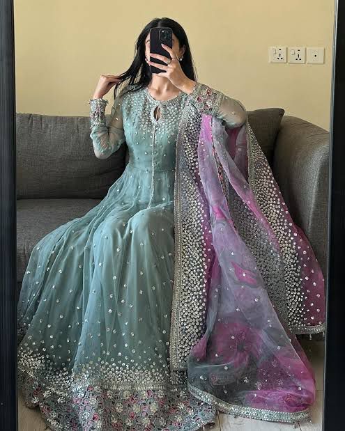 Person wearing a traditional outfit with a teal dress and pink dupatta in a room.