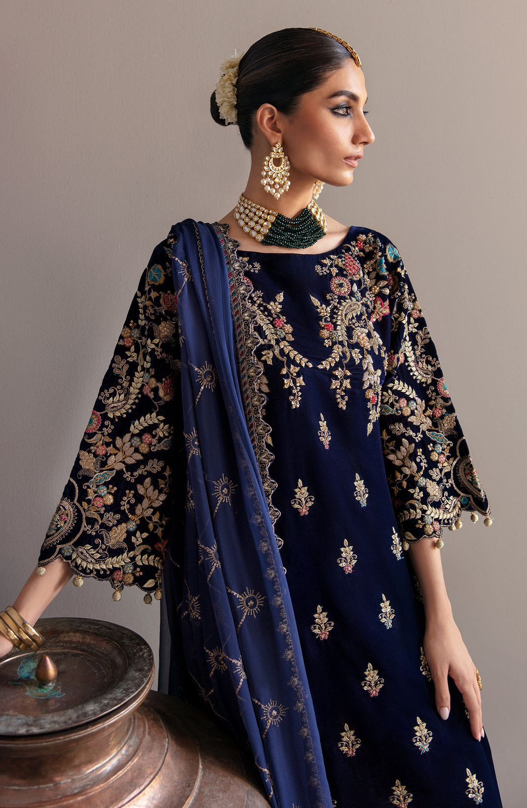 Emaan Adeel Woman wearing a navy blue embroidered outfit with gold details on a gray background