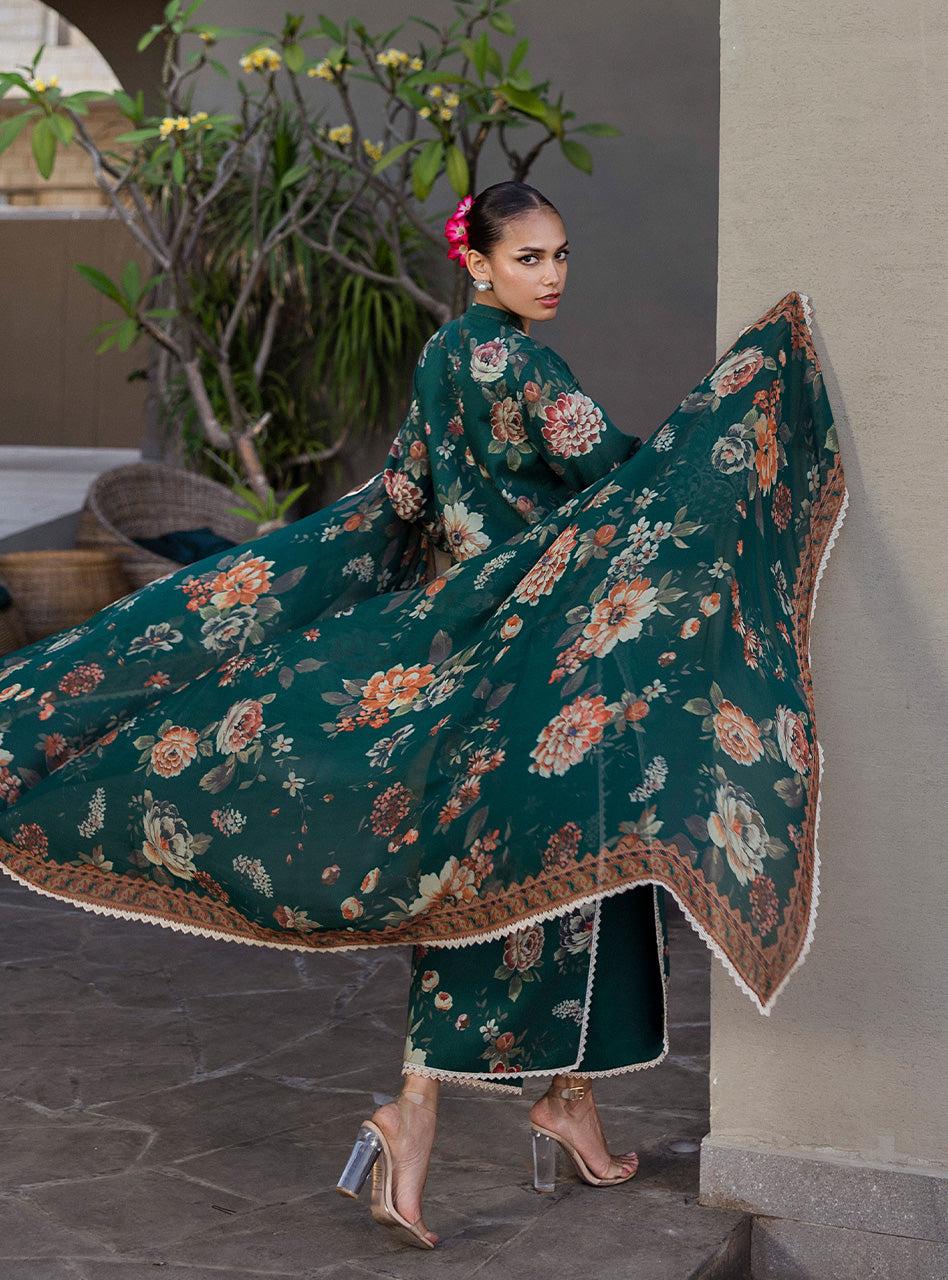 Zainab Chottani PAkistani Dress Woman in a floral dress with a long train, standing indoors with plants in the background.