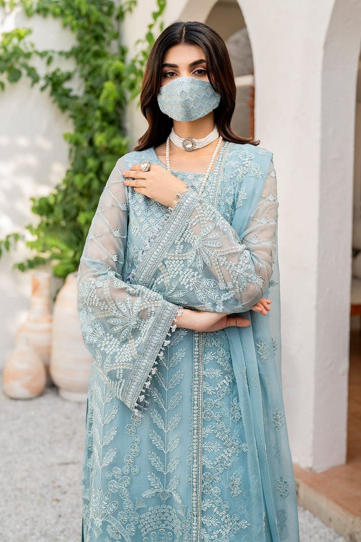 Woman wearing a light blue embroidered traditional outfit with a matching mask indoors.