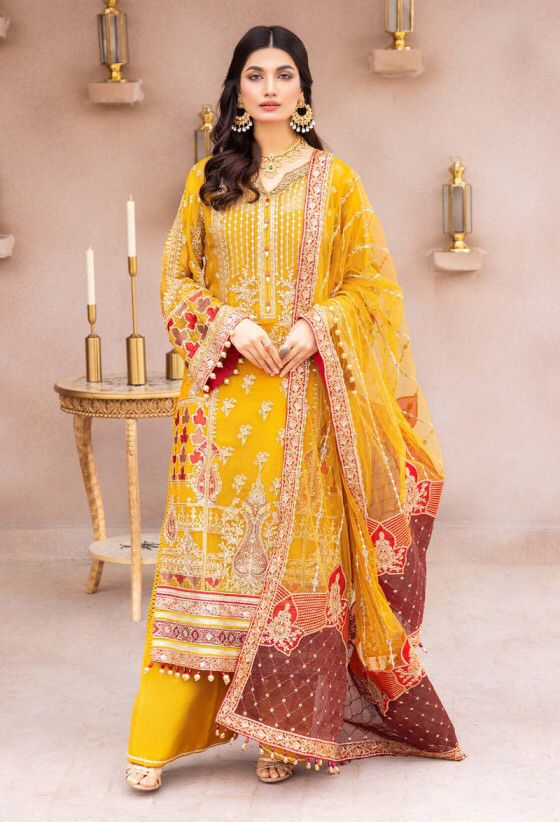 Adan Libas Woman in a yellow and red traditional outfit with intricate patterns, standing in a decorated room.