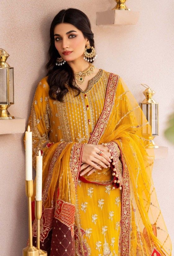 Woman in a yellow and red traditional outfit with intricate patterns, standing against a neutral background.