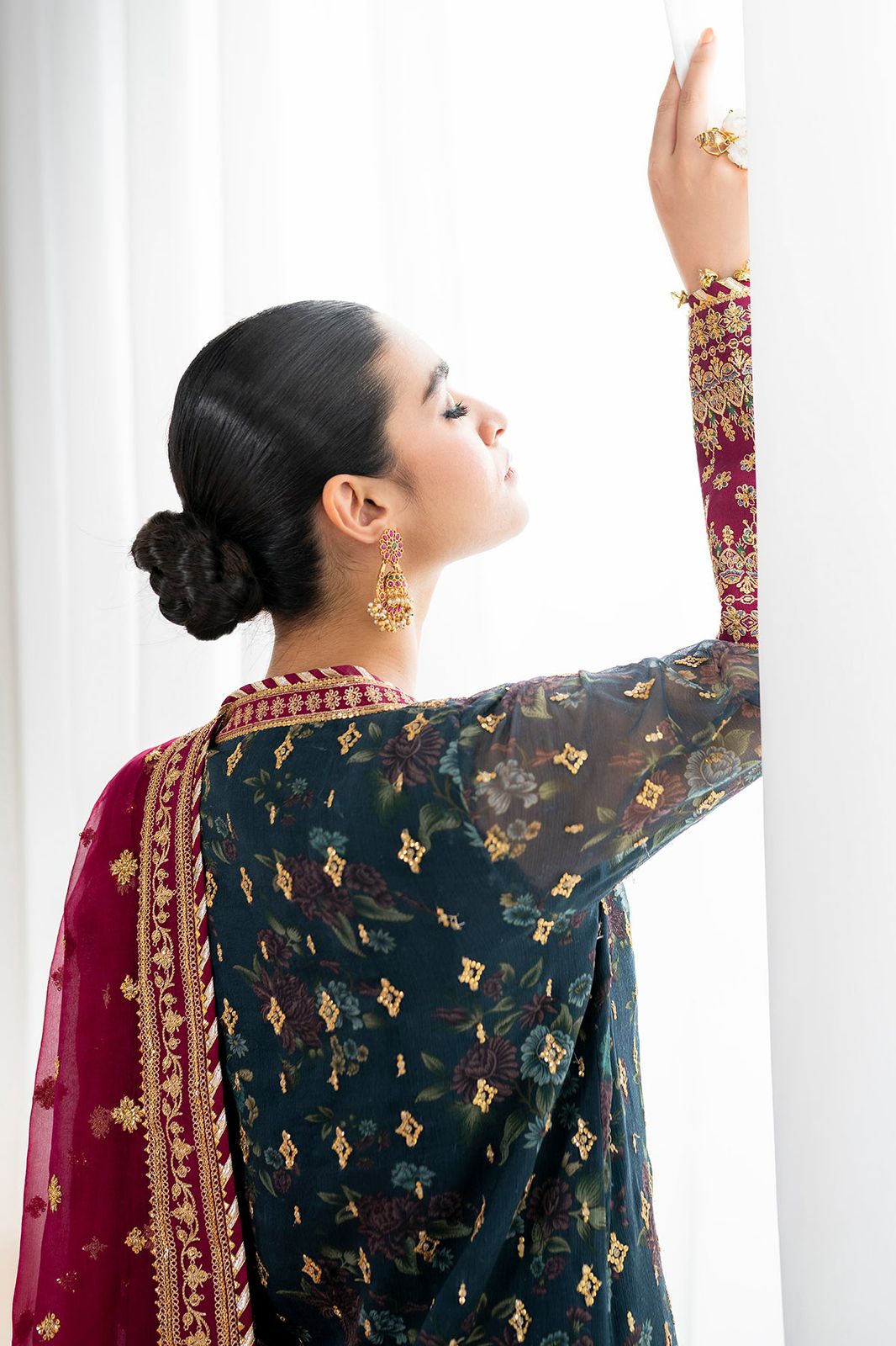 Baroque Perfect For Nikkah wearing a traditional outfit with a floral pattern and red border, standing against a white curtain.