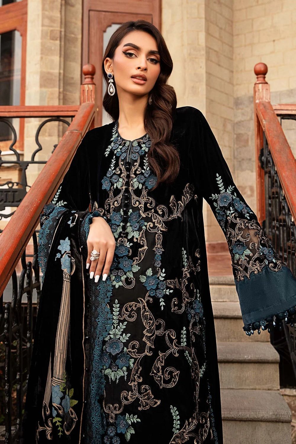 Woman in a black and blue embroidered dress standing on steps outdoors.