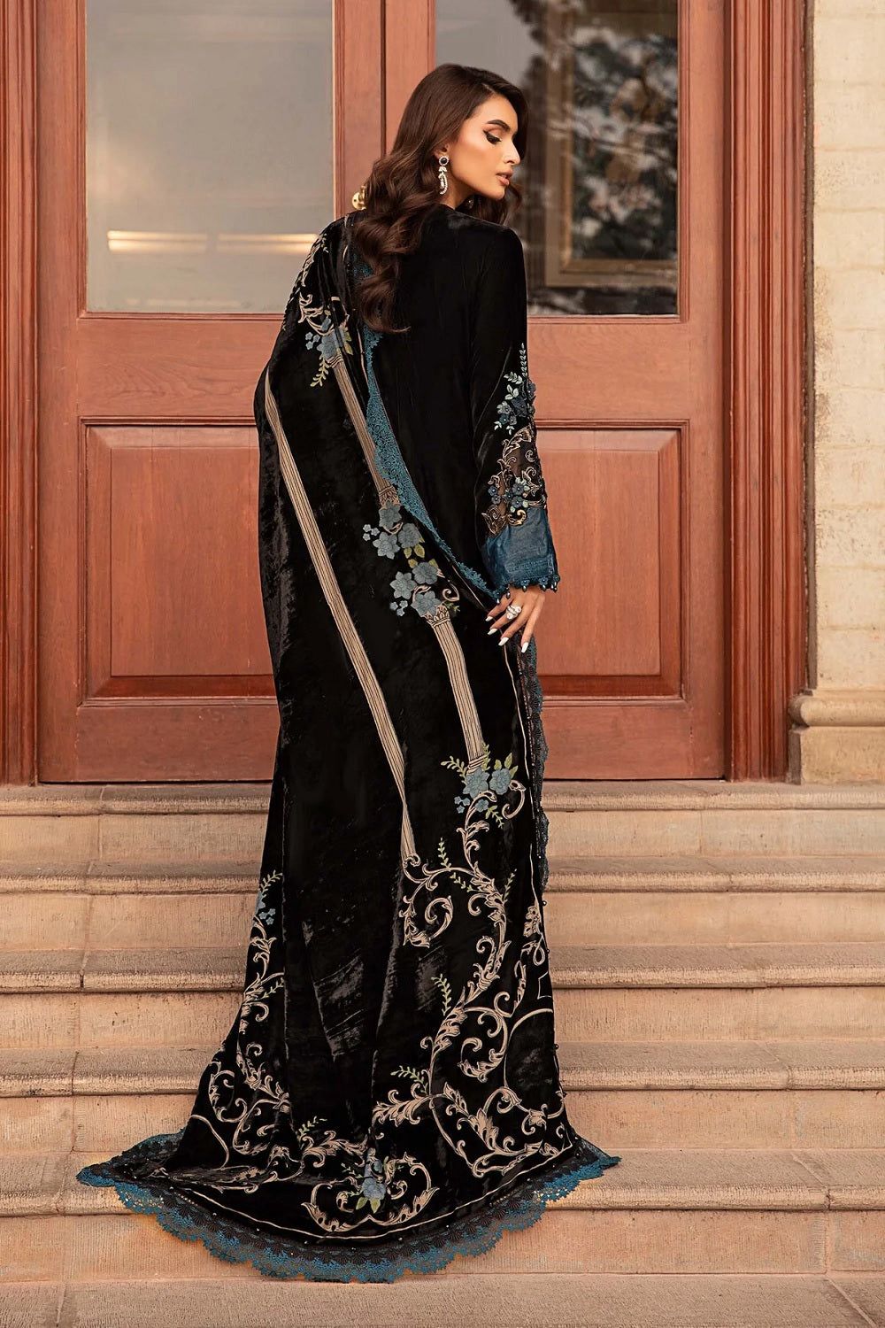 Woman wearing a black embroidered saree with gold details in front of a wooden door.