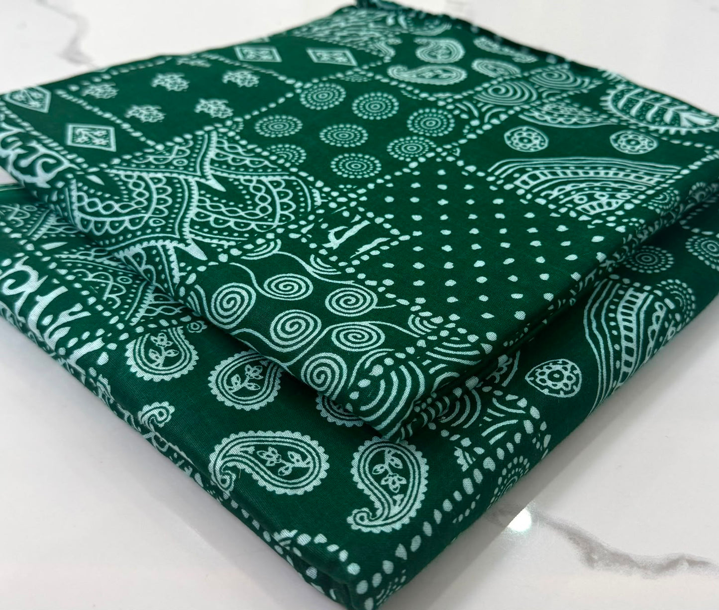A folded dark green fabric item with a white paisley and dot pattern, displayed on a light marble surface.