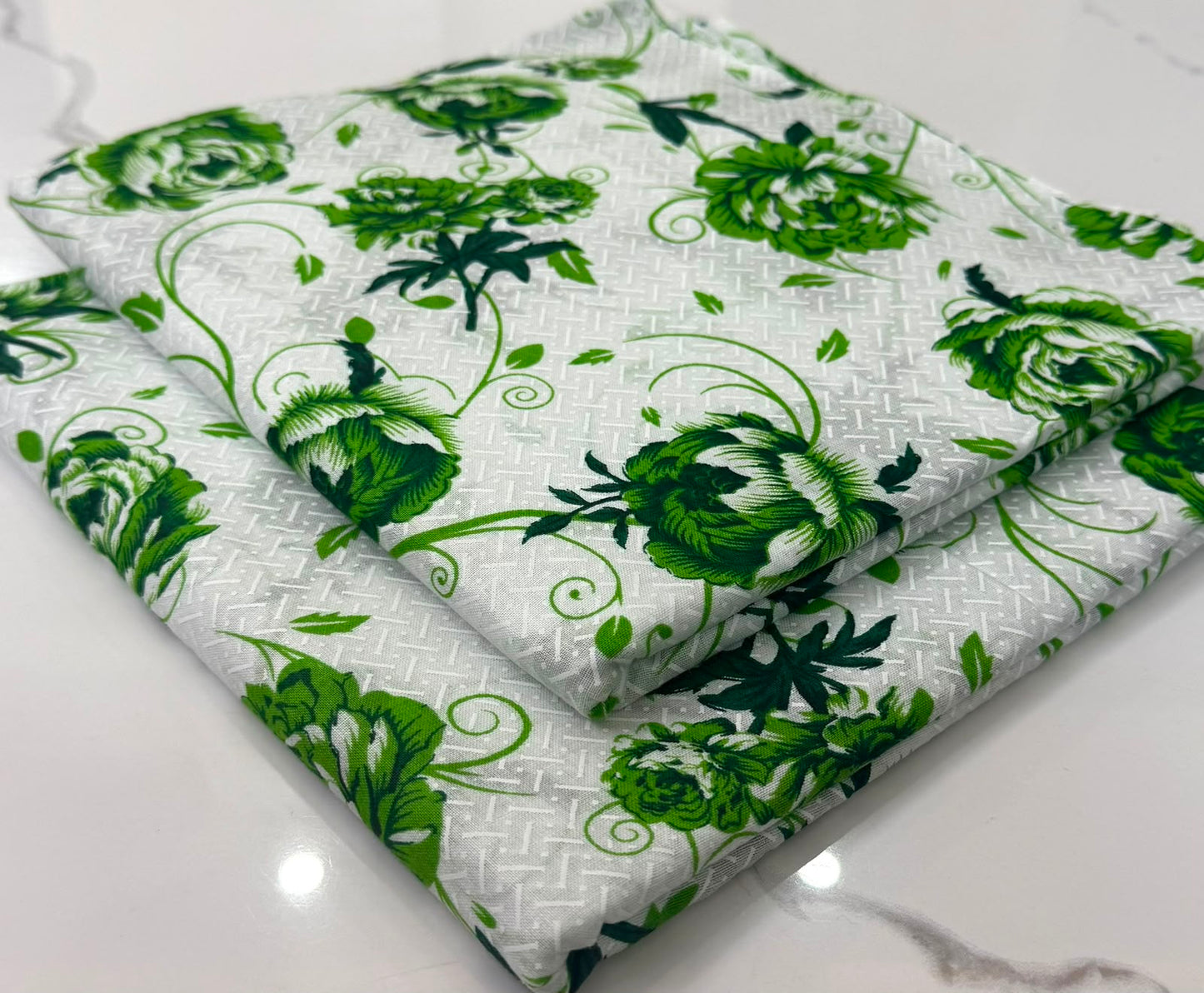 A folded piece of white fabric with a green floral and vine pattern, displayed on a light marble surface.