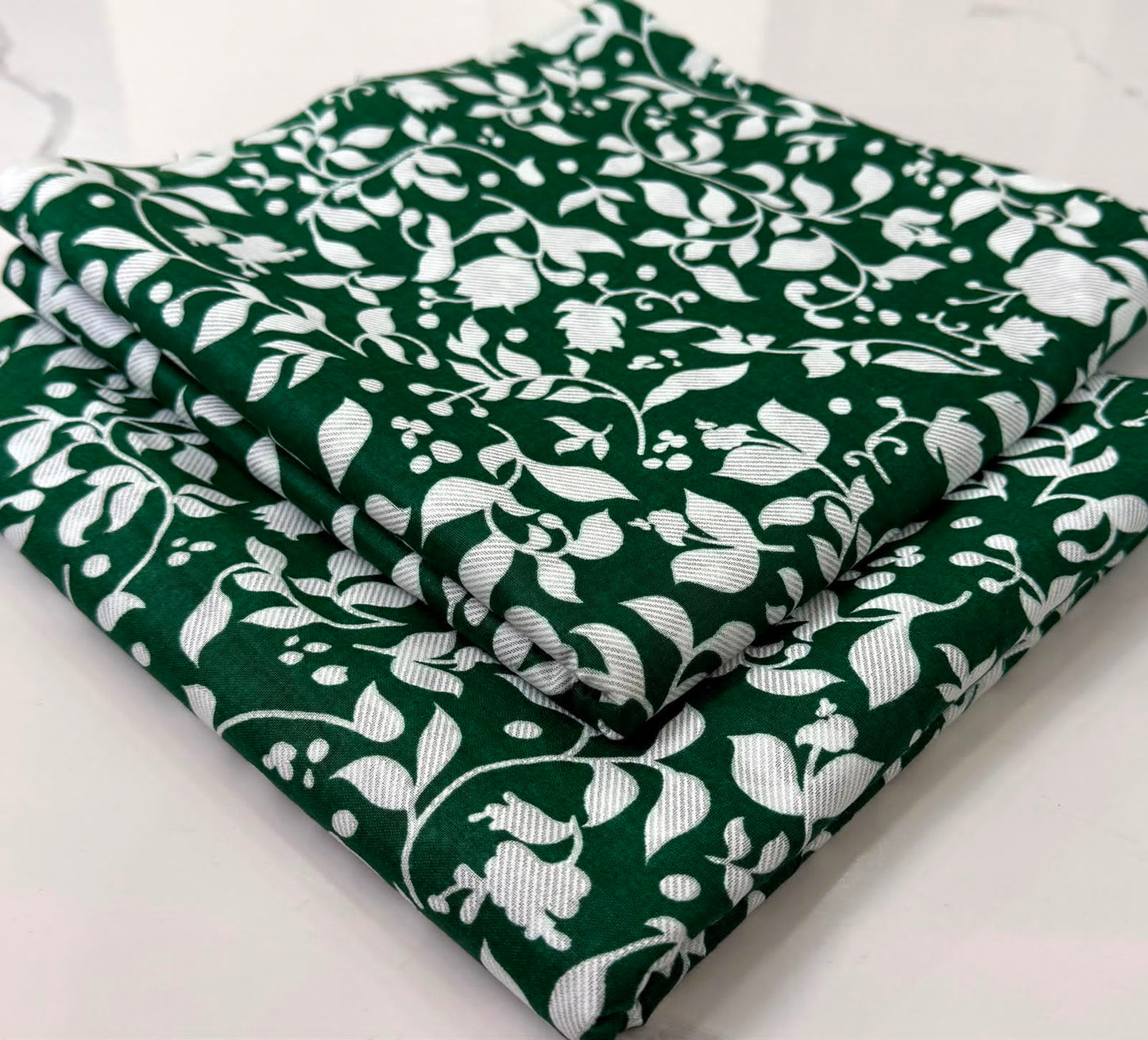 A folded piece of dark green fabric with a white floral and leaf pattern, stacked on a light surface.