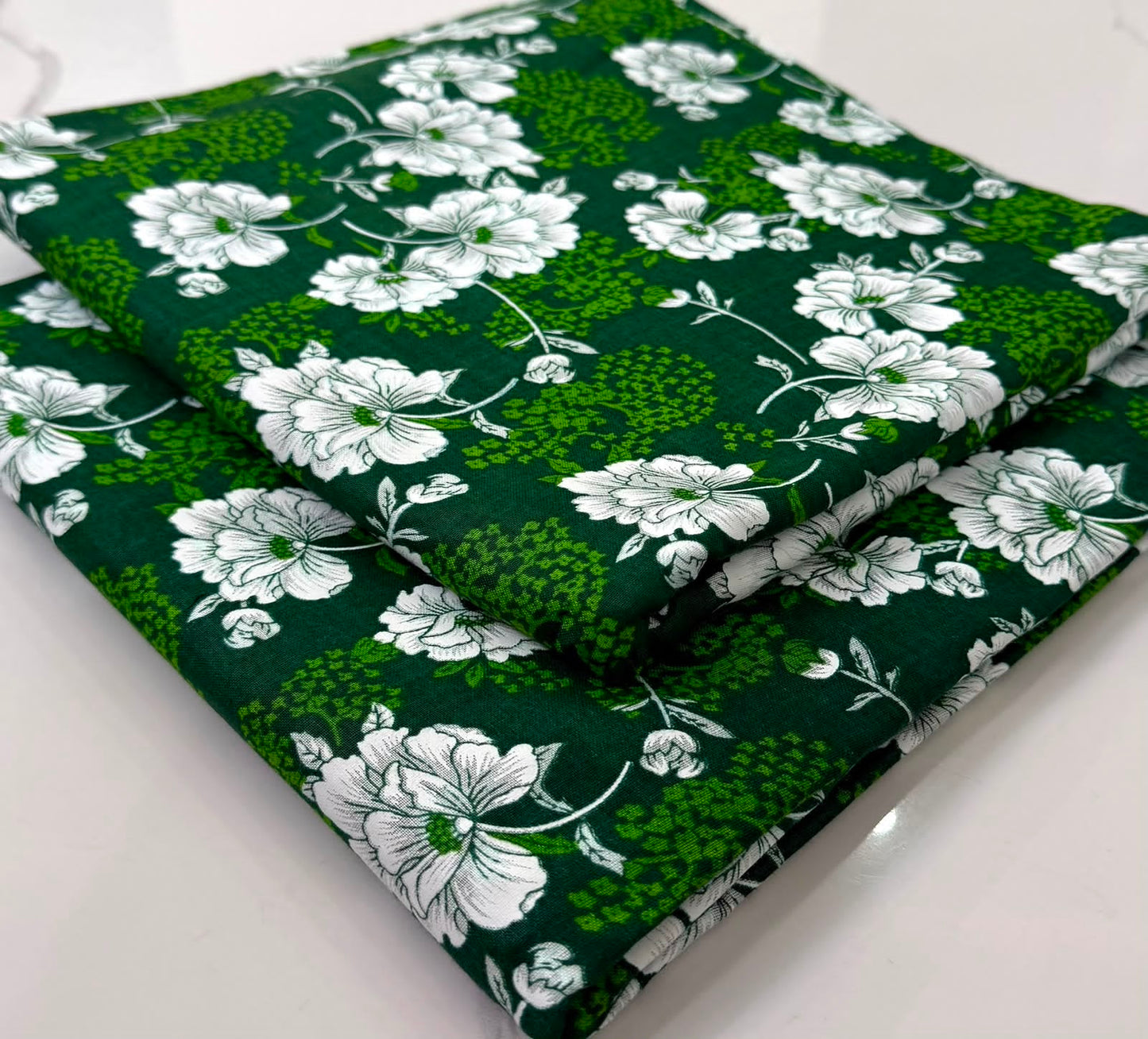A folded piece of dark green fabric with a white floral and leaf pattern, displayed on a clean white surface.