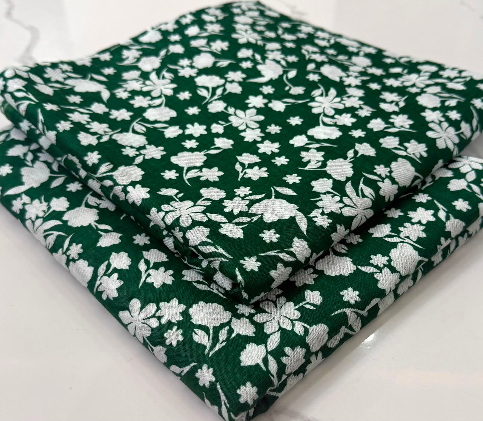 A folded dark green fabric with a white floral pattern, displayed on a light-colored surface.