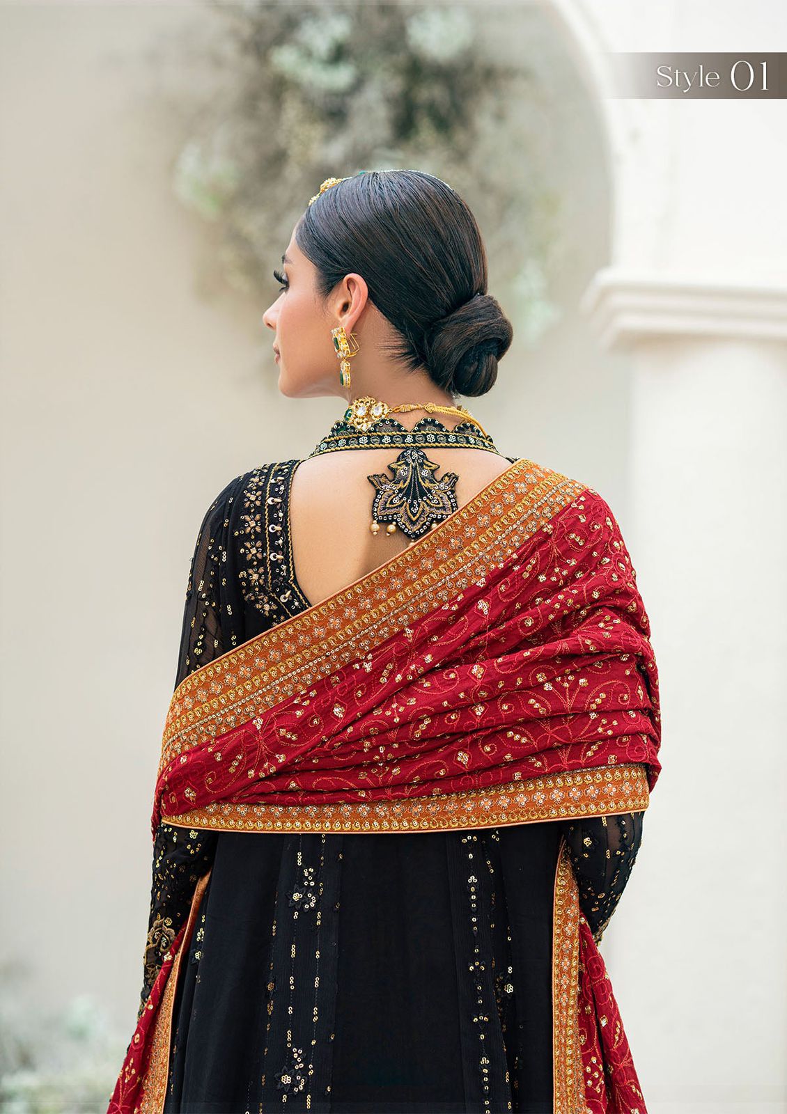 Woman wearing a black and red saree with gold border, standing against a neutral background.