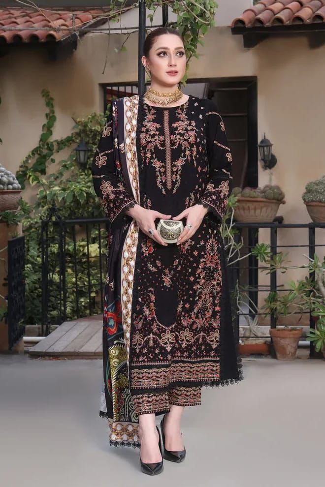 Woman in traditional embroidered outfit standing outdoors with plants and a building in the background