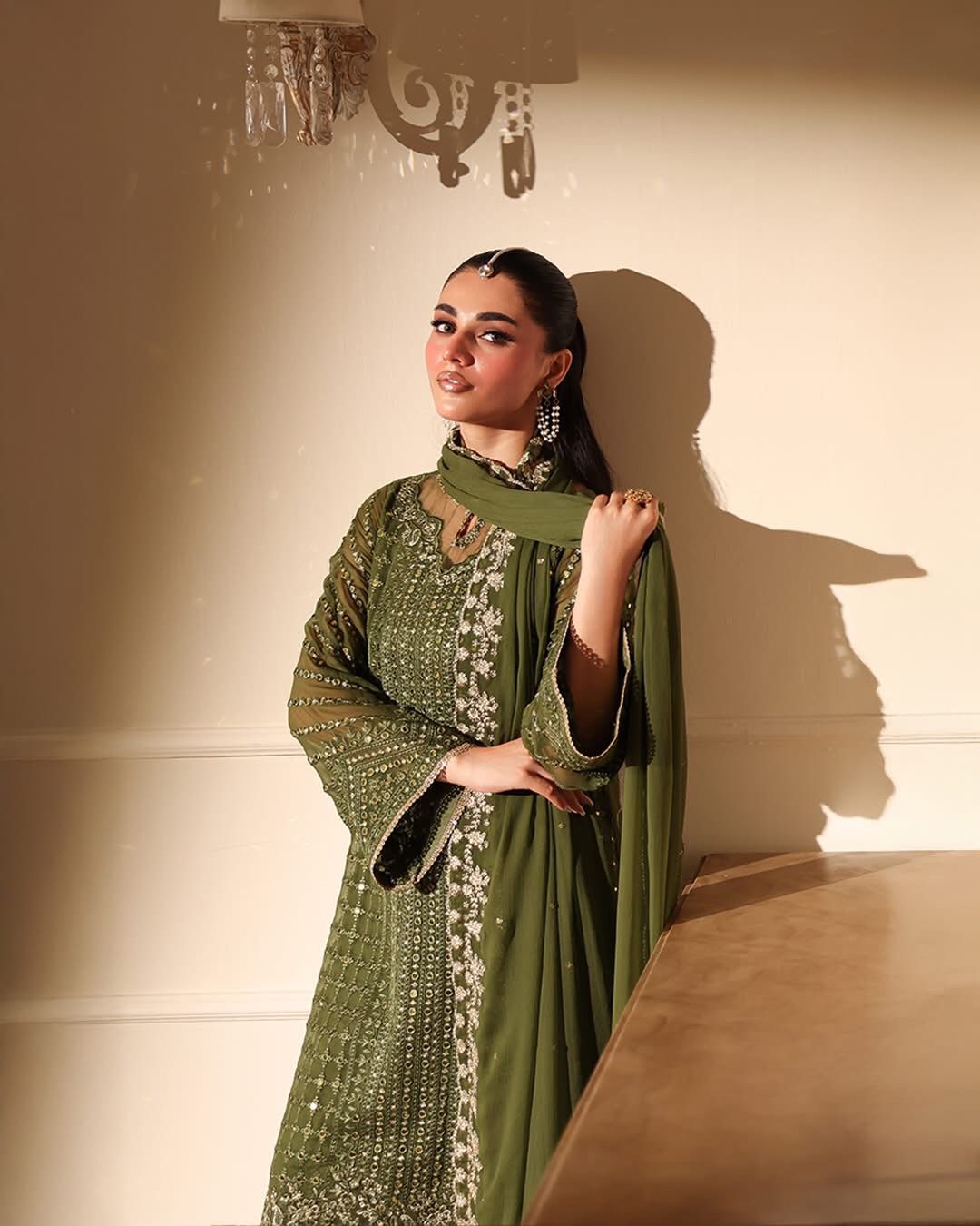 Woman in a green traditional outfit with intricate patterns against a neutral background