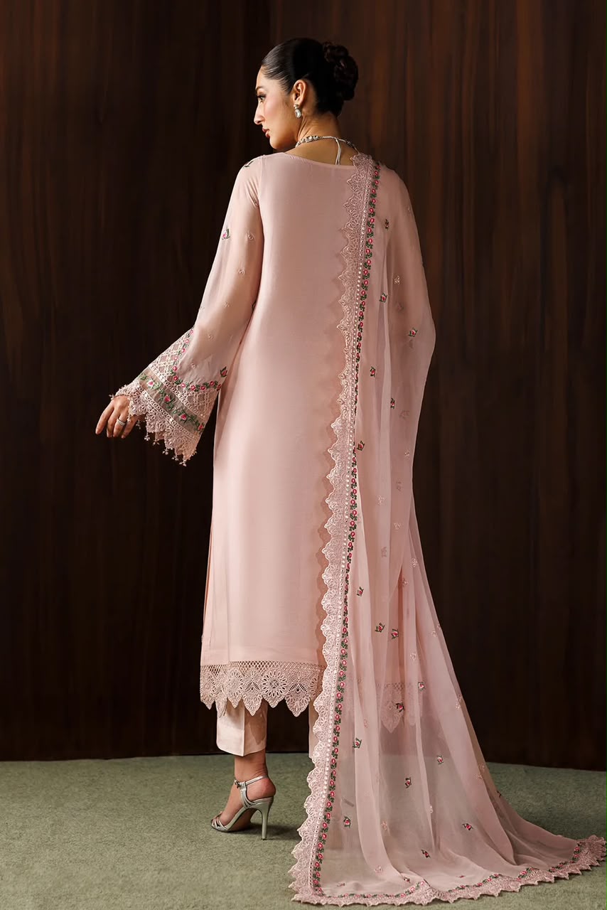 A woman shown from the back wearing a light pink traditional outfit with a long kurta, matching dupatta, and lace-trimmed hem, posed against a dark wood-paneled background.