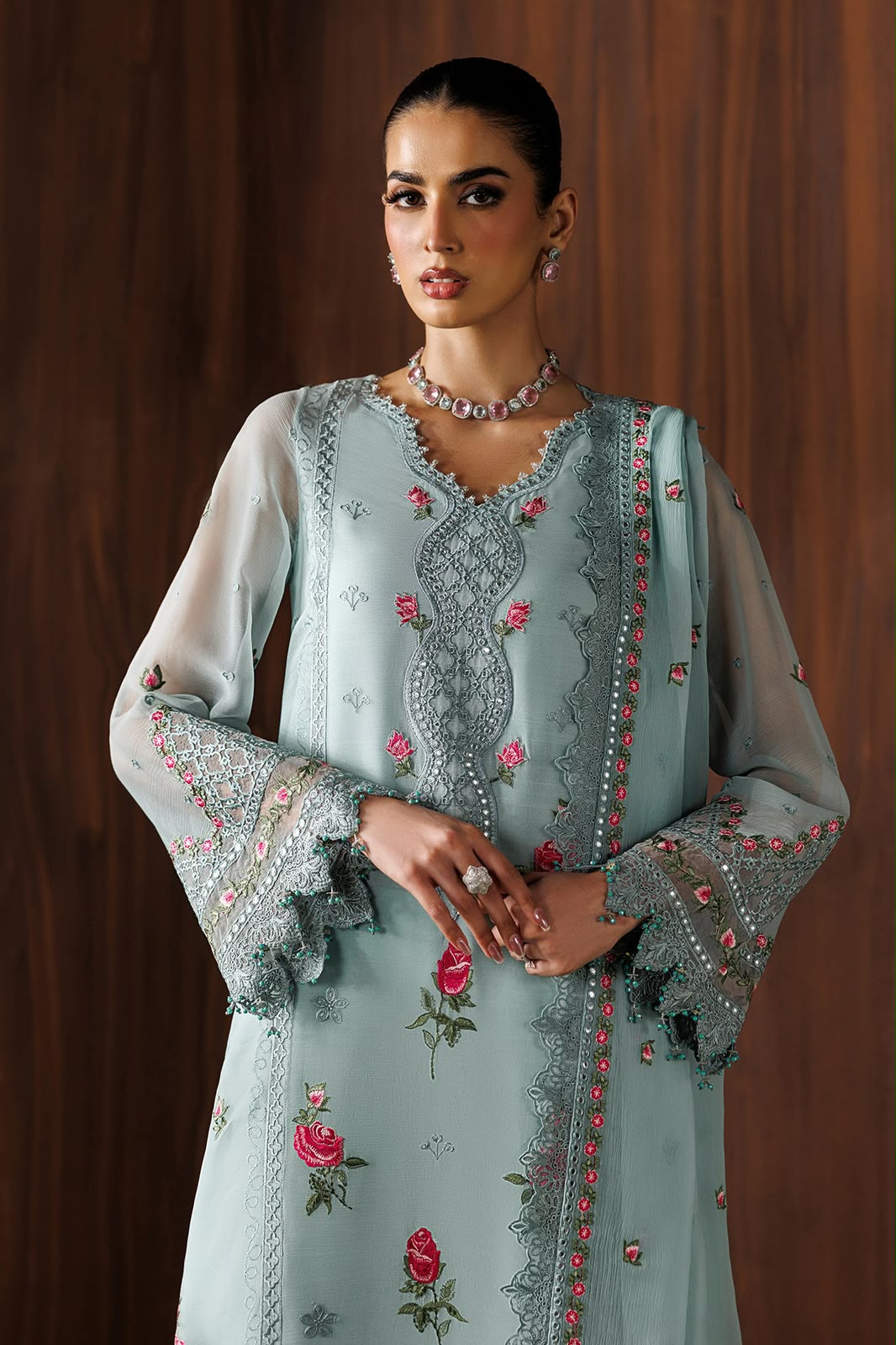 Woman wearing a light blue embroidered dress with floral patterns against a wooden background