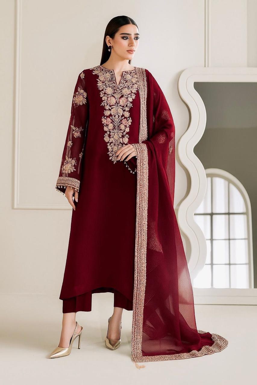 A woman models a deep maroon three-piece traditional outfit with intricate gold and beige floral embroidery on the neckline, sleeves, and border, paired with a matching sheer dupatta.