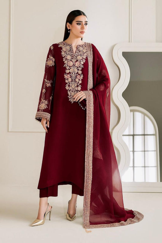 A woman models a deep maroon three-piece traditional outfit with intricate gold and beige floral embroidery on the neckline, sleeves, and border, paired with a matching sheer dupatta.