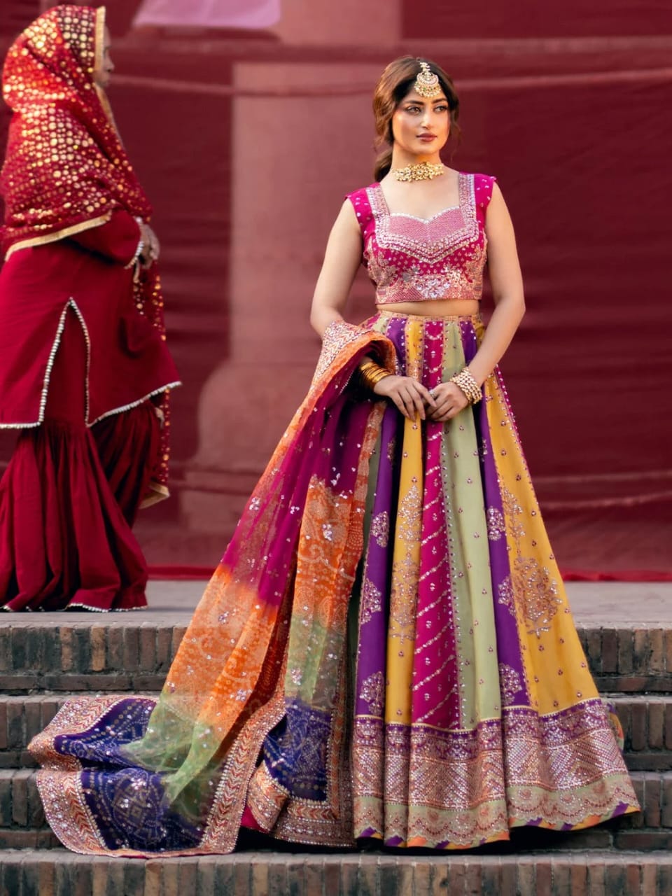 Woman in a colorful traditional outfit standing on steps with another person in the background.