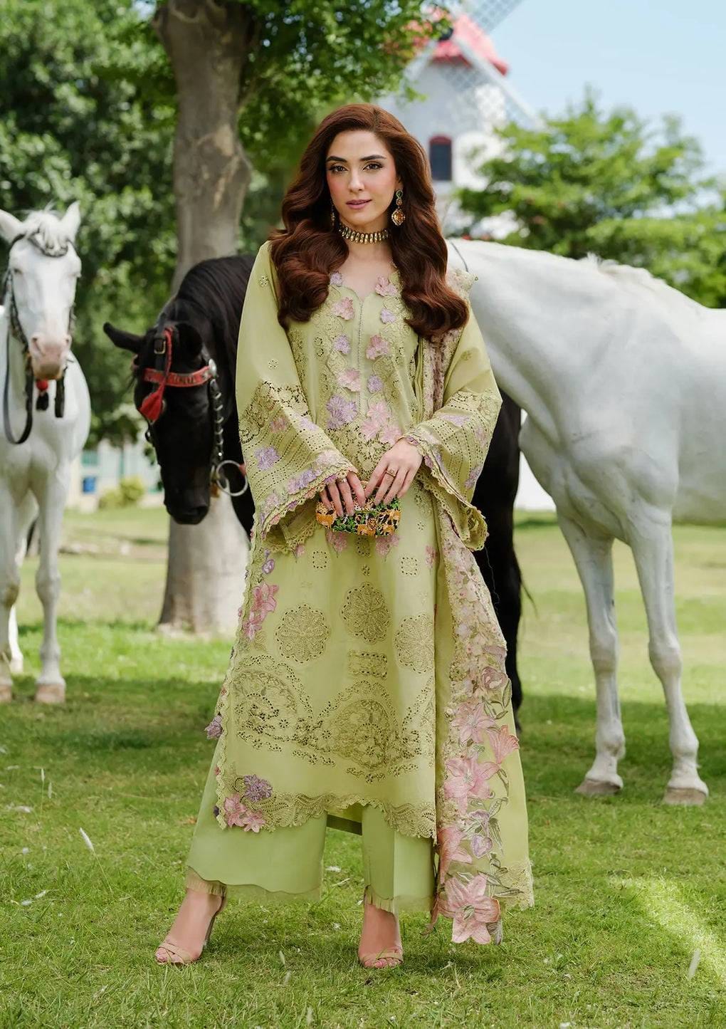Woman in a light green embroidered outfit standing in front of horses in a park-like setting
