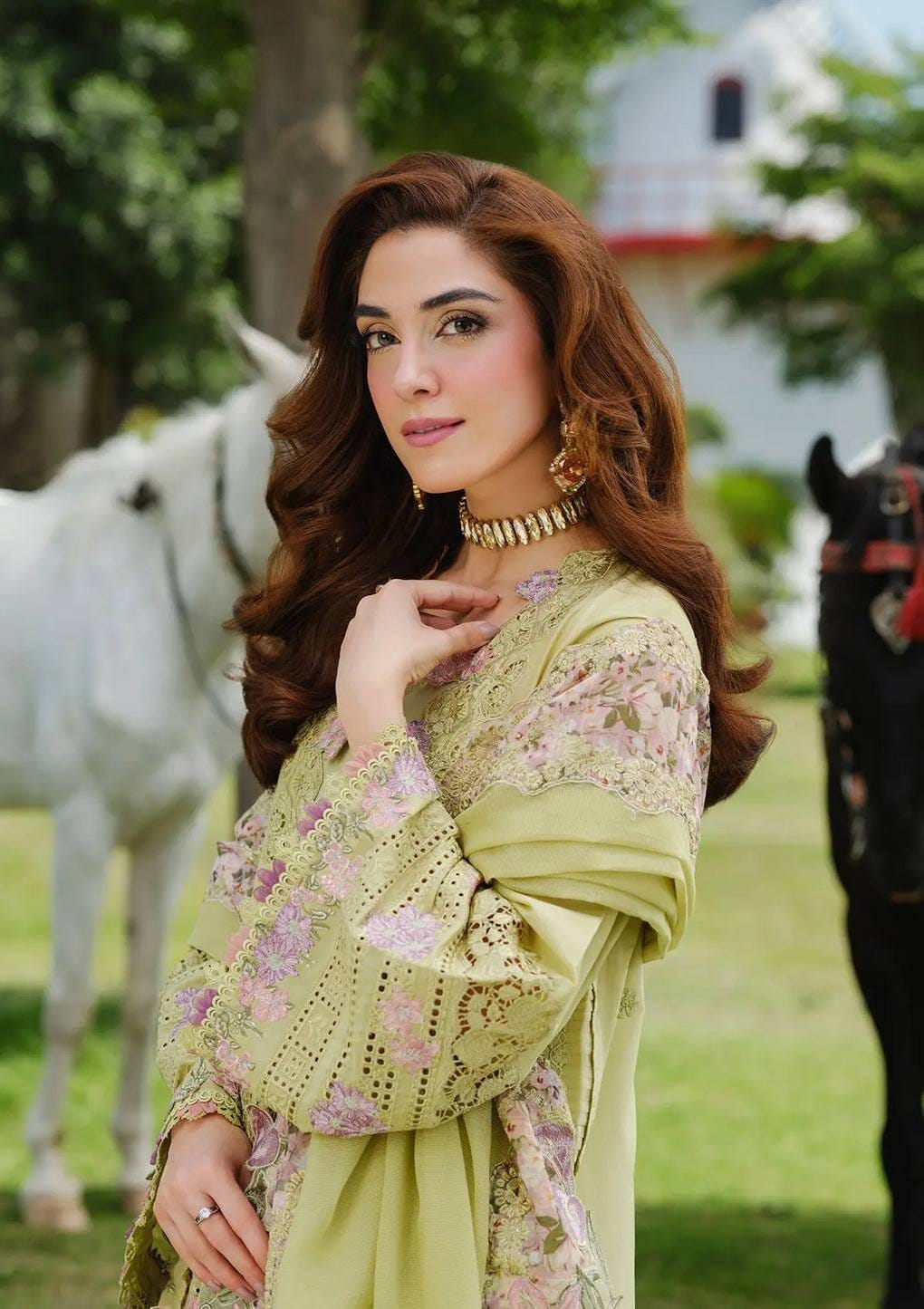Woman in a floral dress standing outdoors with horses in the background
