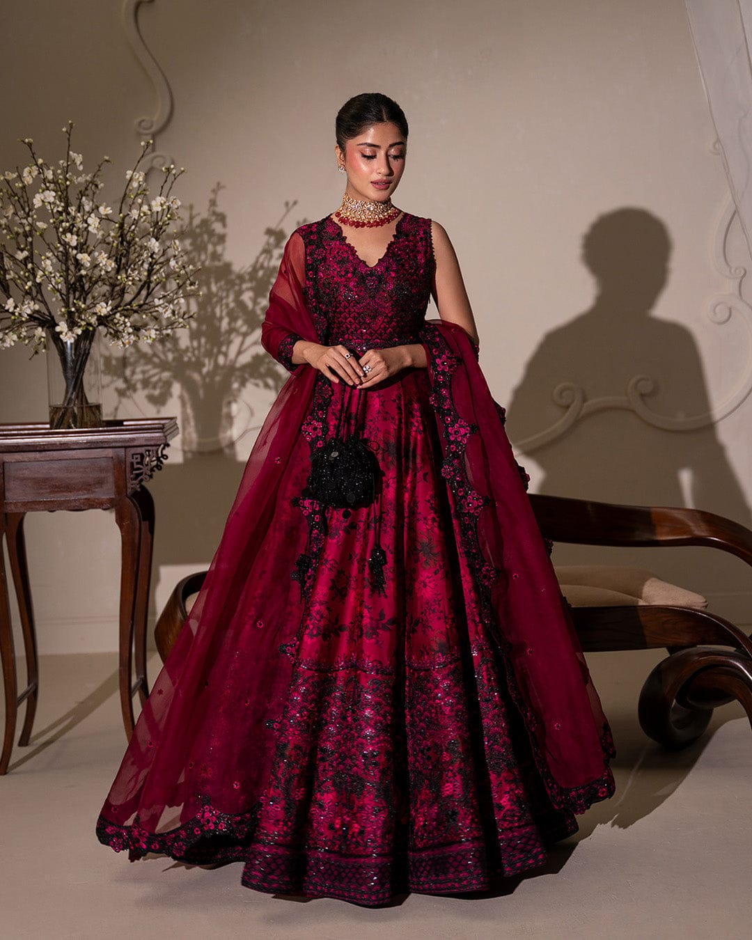 Woman in a burgundy evening gown with floral patterns in a decorated room.