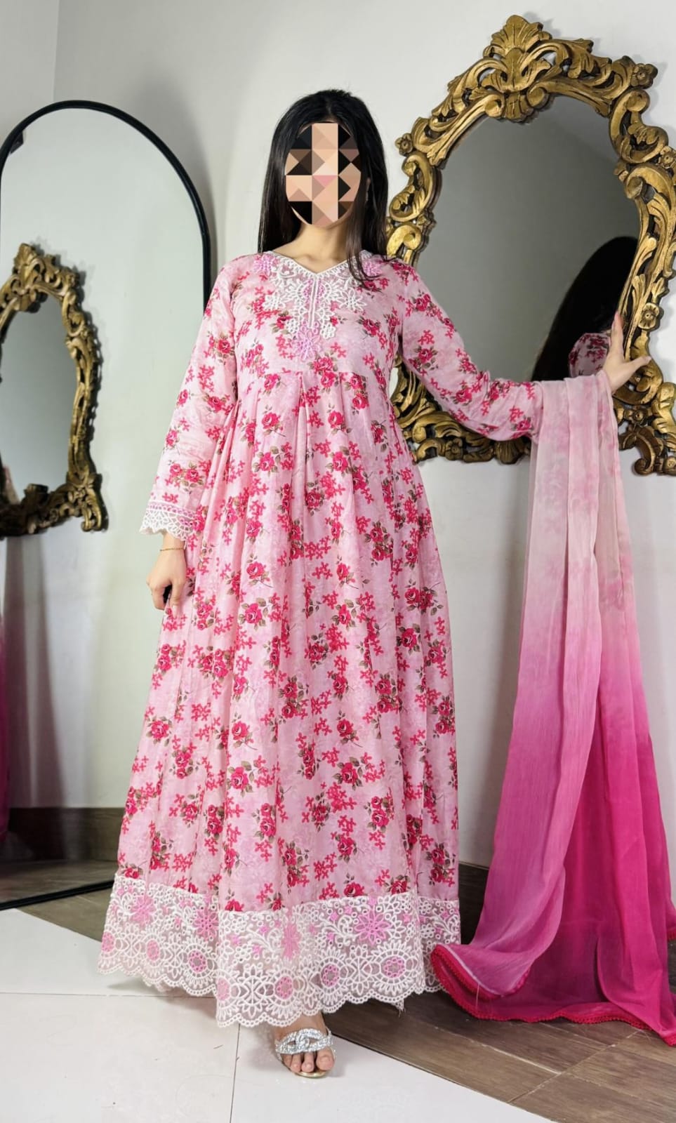 Woman wearing a pink floral dress with a matching dupatta in front of decorative mirrors.