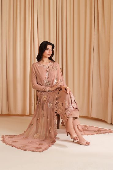 Woman in a pink embroidered outfit sitting against a beige curtain.