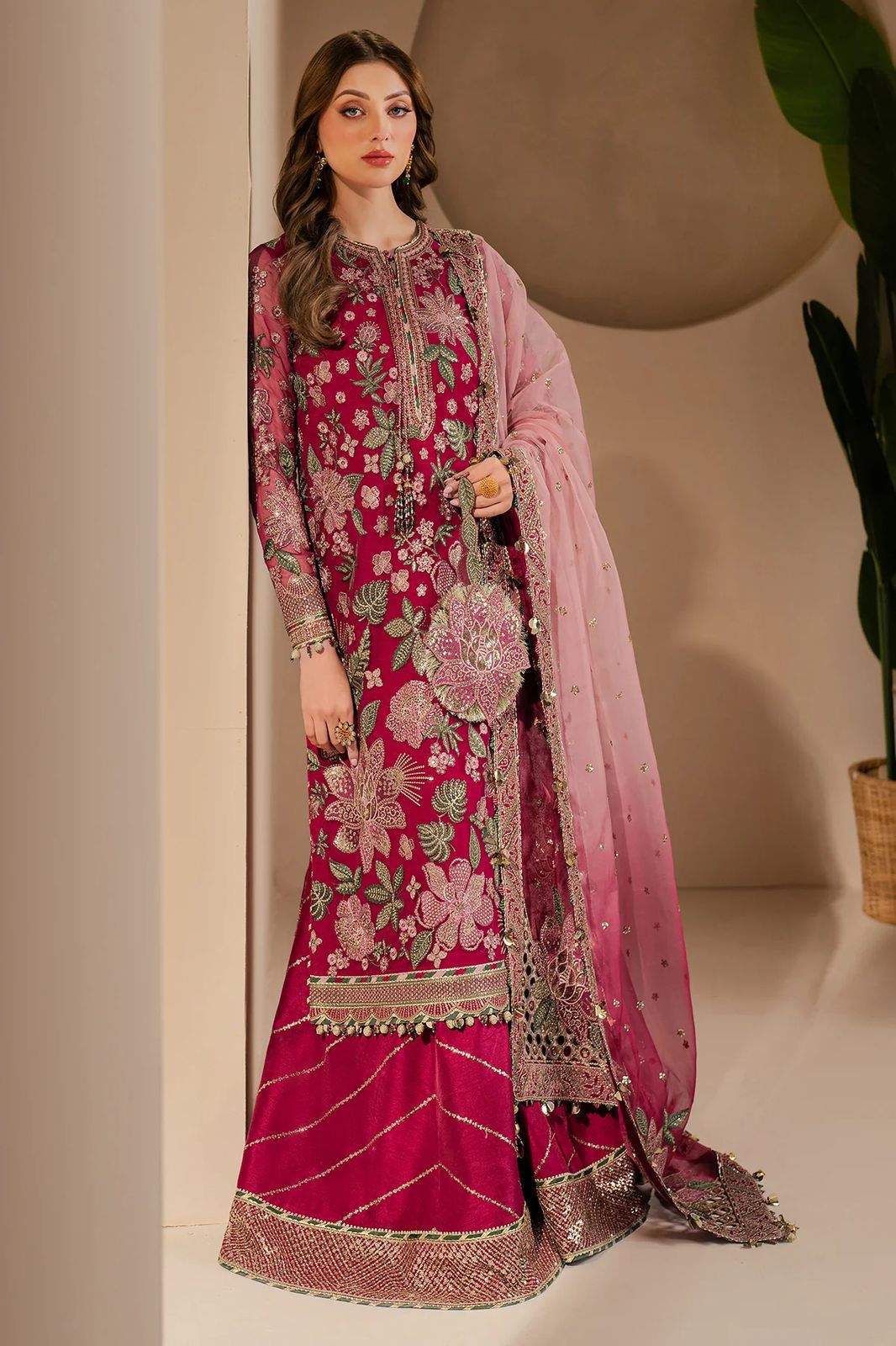 Woman wearing a pink embroidered traditional outfit with a matching dupatta against a neutral background