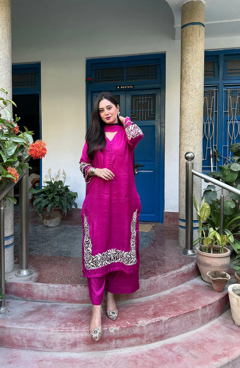 Woman in a bright pink traditional outfit standing on steps with a blue door and plants in the background