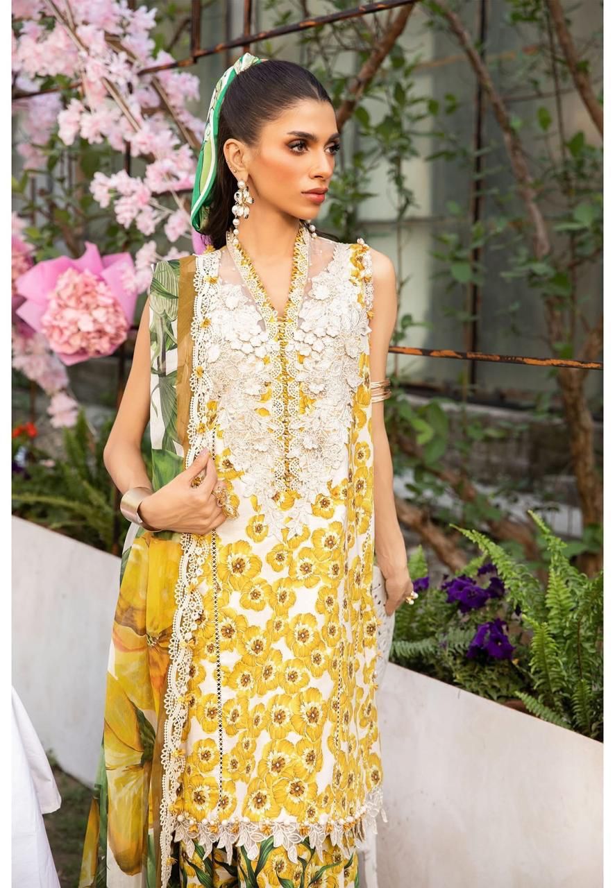 Woman wearing a yellow and white floral dress with a green headscarf, standing outdoors with flowers in the background.