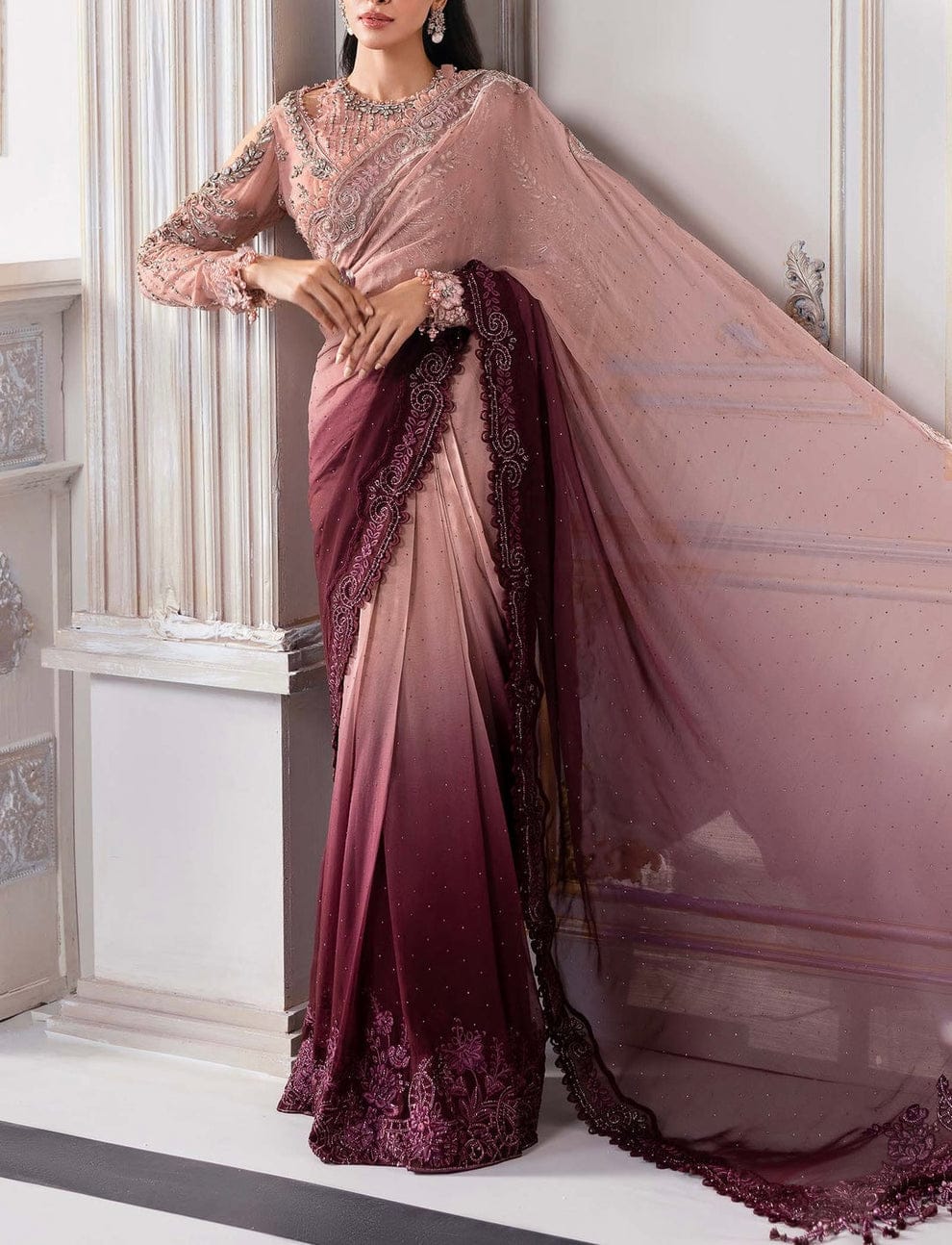 Woman wearing a pink and purple saree with intricate designs in a decorative setting.