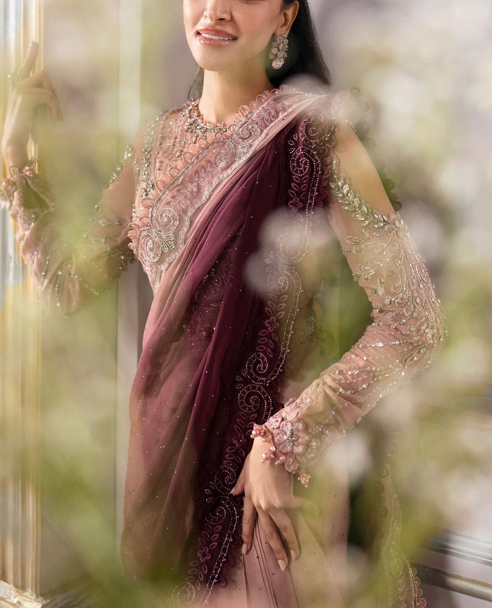 Woman wearing a traditional maroon saree with intricate designs, standing amidst greenery.