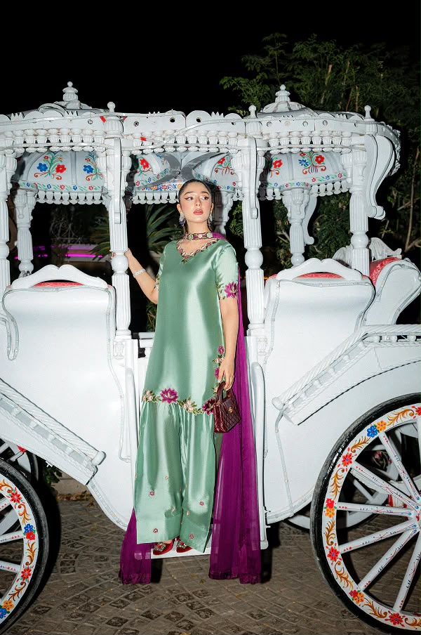 Woman in a green and purple traditional outfit standing in front of a white decorated vehicle.
