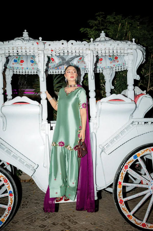 Woman in a green and purple traditional outfit standing in front of a white decorated vehicle.