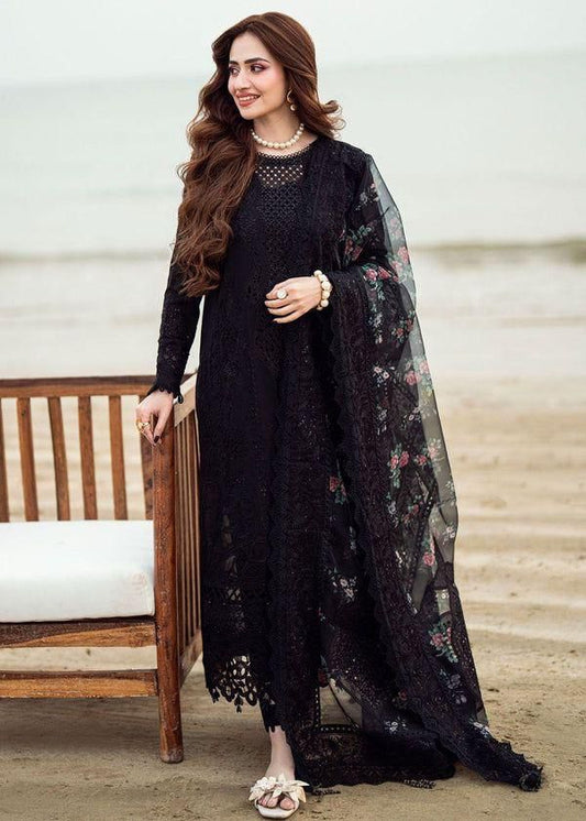Nureh Black Sana Jawedtraditional outfit with a floral dupatta sitting on steps.