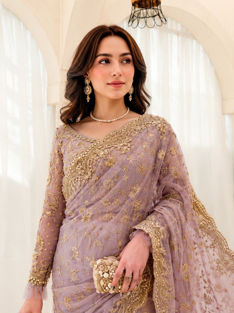 A woman wearing a lavender and gold embroidered traditional outfit with a matching dupatta, holding a decorative gold clutch in a bright indoor setting with arched windows and white curtains.