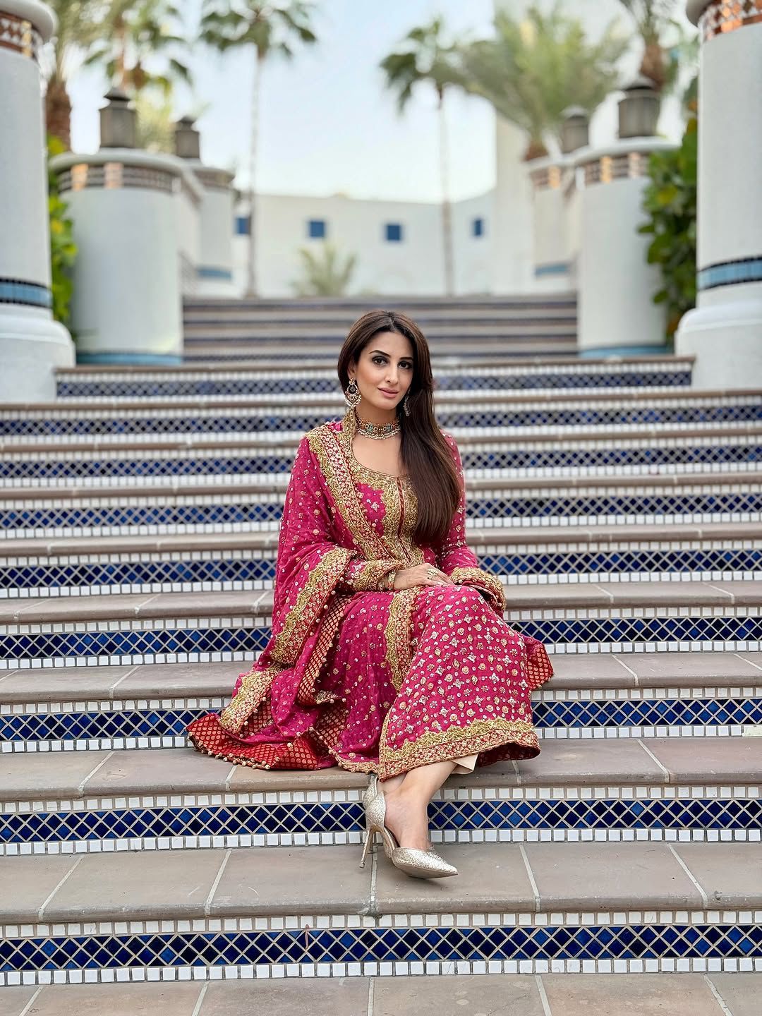 Woman in a pink traditional outfit sitting on steps with palm trees in the background
