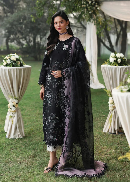 Woman in a black and purple traditional outfit standing outdoors with floral decorations.