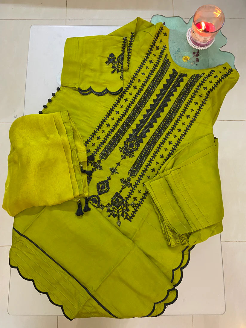 Green embroidered garment on a white surface with a candle in the background