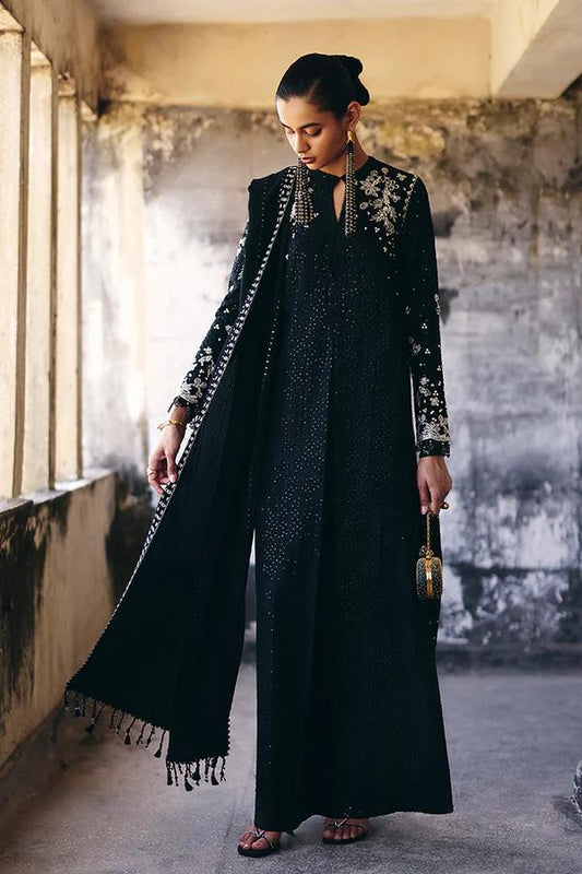 Woman in a black outfit with intricate detailing standing in an industrial setting.