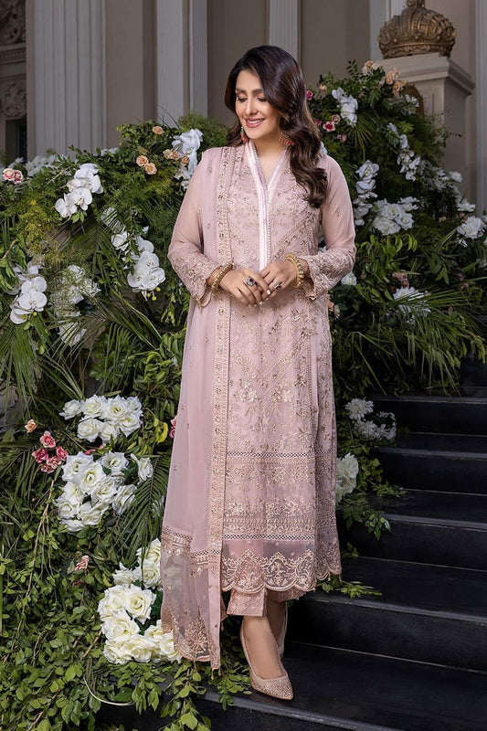 Woman in a pink embroidered outfit standing in front of floral decorations.