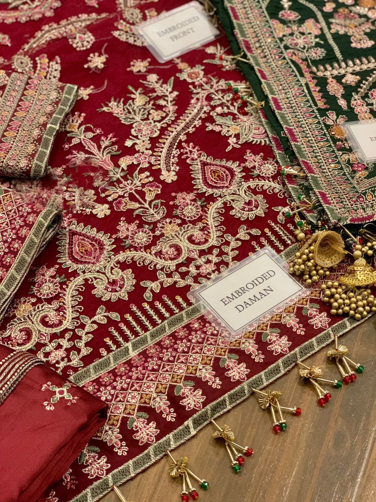 Embroidered daman fabric with gold and green patterns on a wooden surface