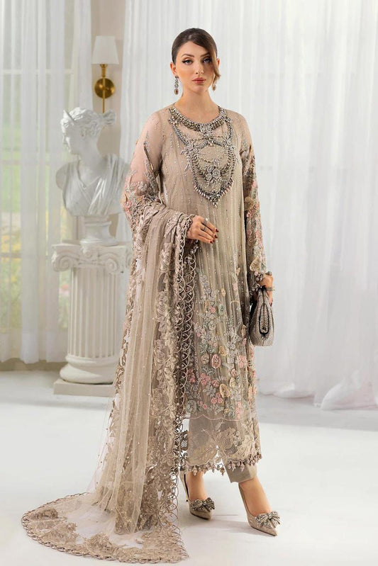 MAria b Wedding Pakistani Dress Woman in a beige embroidered outfit standing in a room with white curtains and a statue.